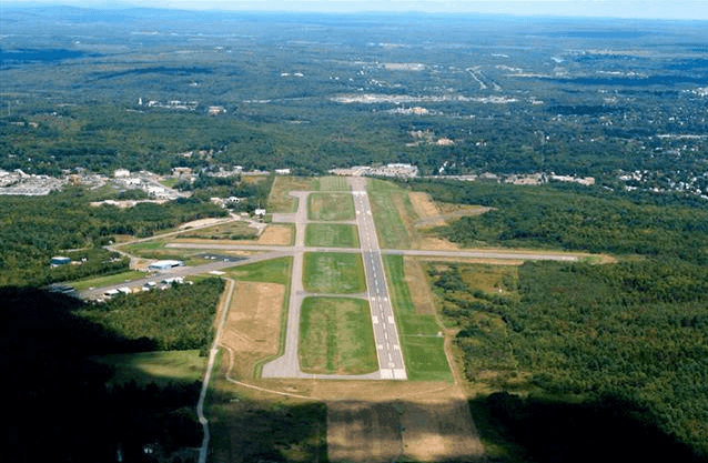 Aerial view of a rural airport runway surrounded by green forests and landscape.